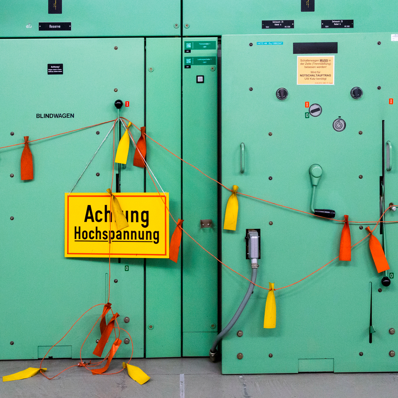 Türkisgrüne Anlage an der bunte Sicherheits-Fähnchen sowie ein Schild Achtung Hochspannung hängen.