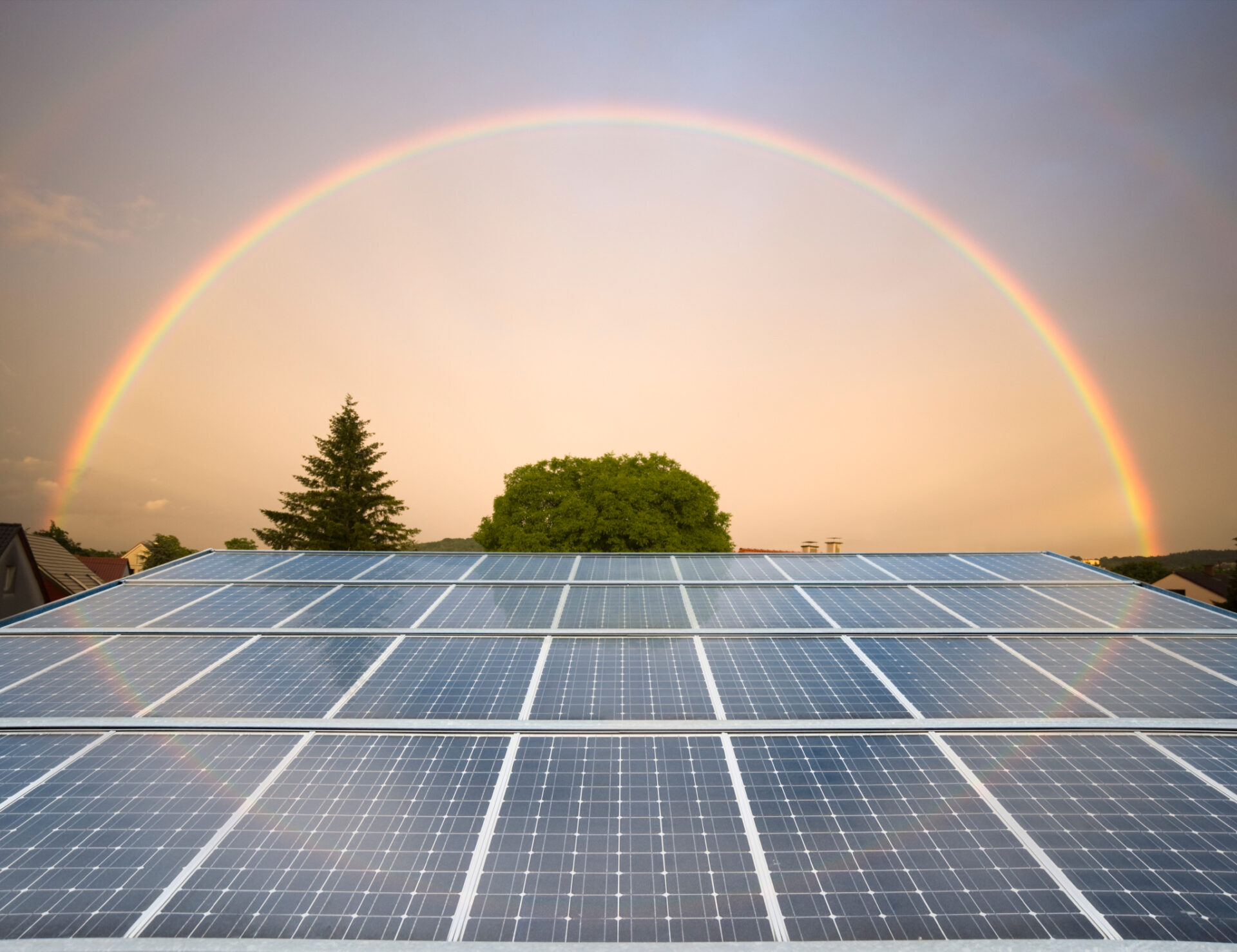 Ein Hausdach, das aus Solarpannels besteht. Im Hintergrund ist ein Regenbogen zu sehen.