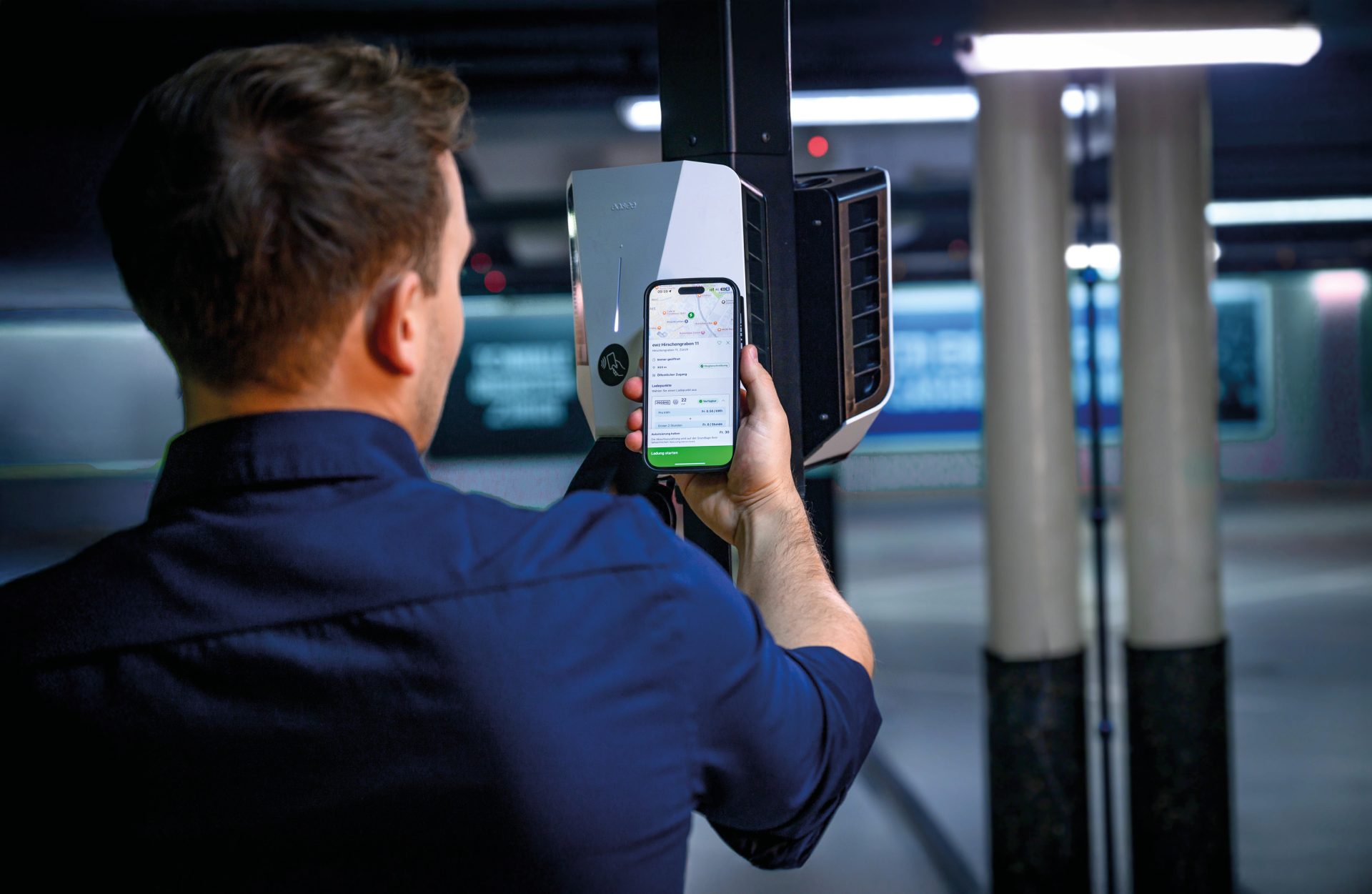 Ein Mitarbeiter prüft per Smartphone-App den Status einer vernetzten Ladestation – Teil eines digitalen Lademanagementsystems zur effizienten Steuerung von Stromflüssen und zur Sicherstellung der Stabilität im Stromnetz für eine zuverlässige Energieversorgung.