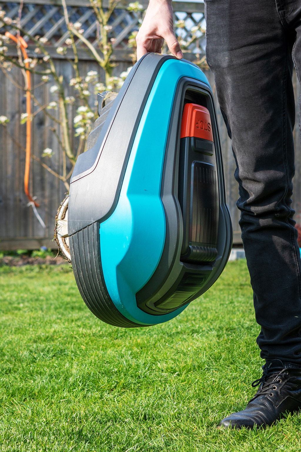Mann trägt Mähroboter im Garten – typischer Stromfresser im Garten und versteckter Stromverbraucher.